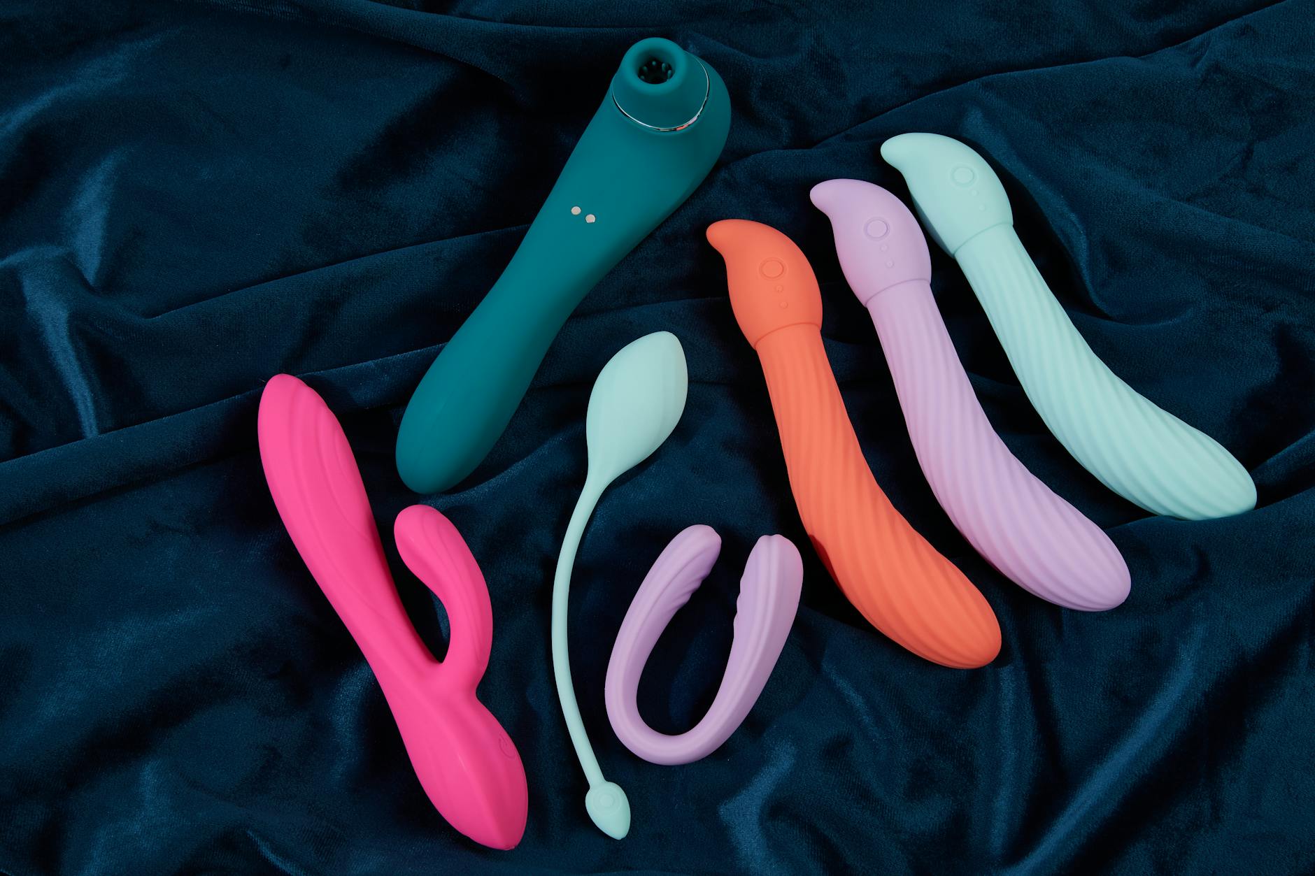 Eine Hand hält einen blauen Silikonvibrator gegen einen violetten Hintergrund, was Selbstliebe und Sexualität fördert