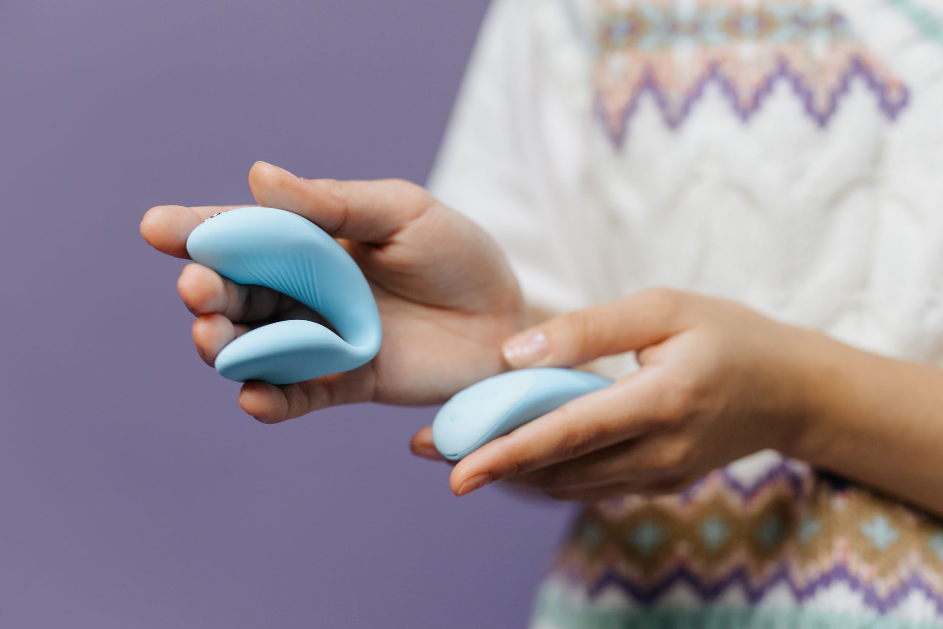Nahaufnahme von Händen, die einen schlanken blauen Vibrator gegen einen violetten Hintergrund halten