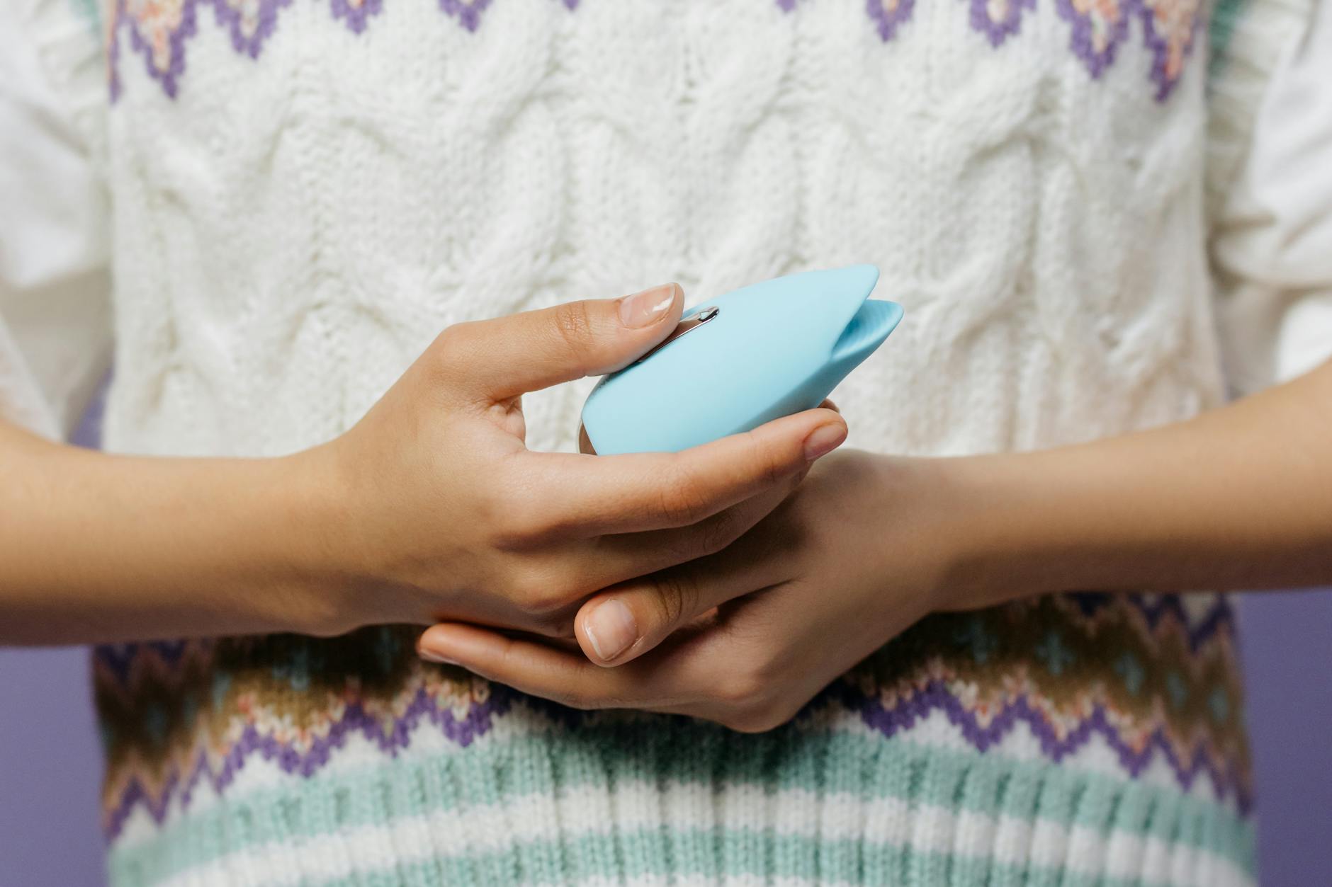 Hand, die einen blauen persönlichen Massager gegen einen gestrickten Pullover hält.