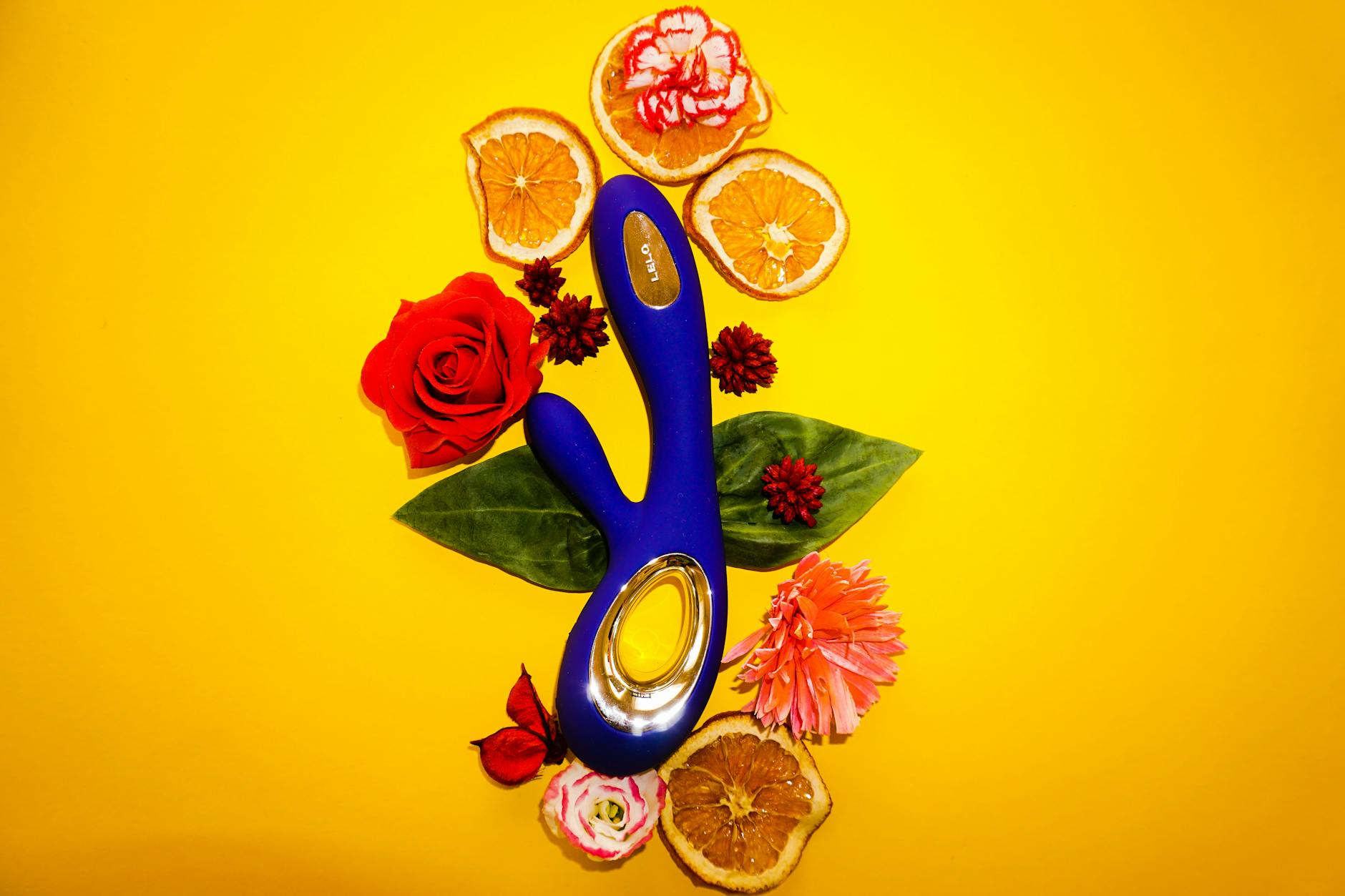 A lemon clitoral vibrator surrounded by flowers and citrus slices on a soothing yellow background