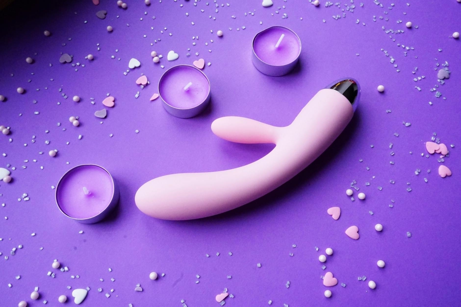 Rosa Vibrator auf violettem Hintergrund mit Herzenkonfetti und Kerzen für romantische Atmosphäre